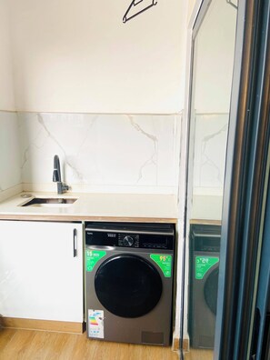 A compact kitchen with a built-in washing machine, a sink, and a mirror. - Cozy 1-bedroom apartment in lovely Kilimani with gym (Nairobi)