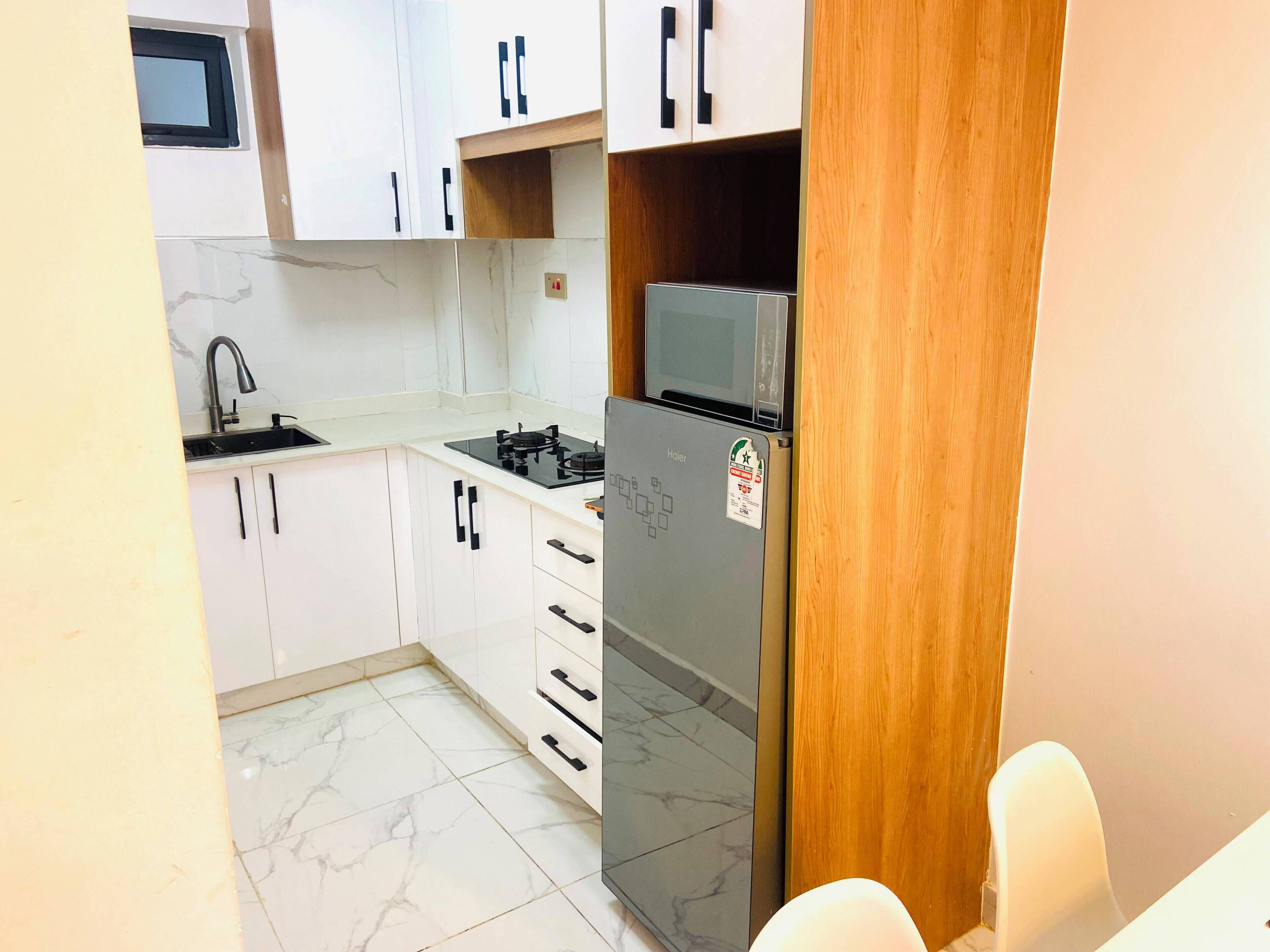 A compact kitchen with white cabinets, a stainless steel sink, a built-in microwave, and a refrigerator.