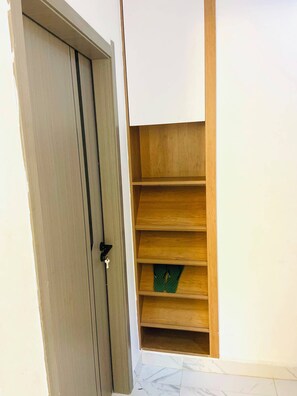 Eine geschlossene Tür mit Schlüsselloch, ein Holzregal mit mehreren Fächern und ein Fliesenboden.