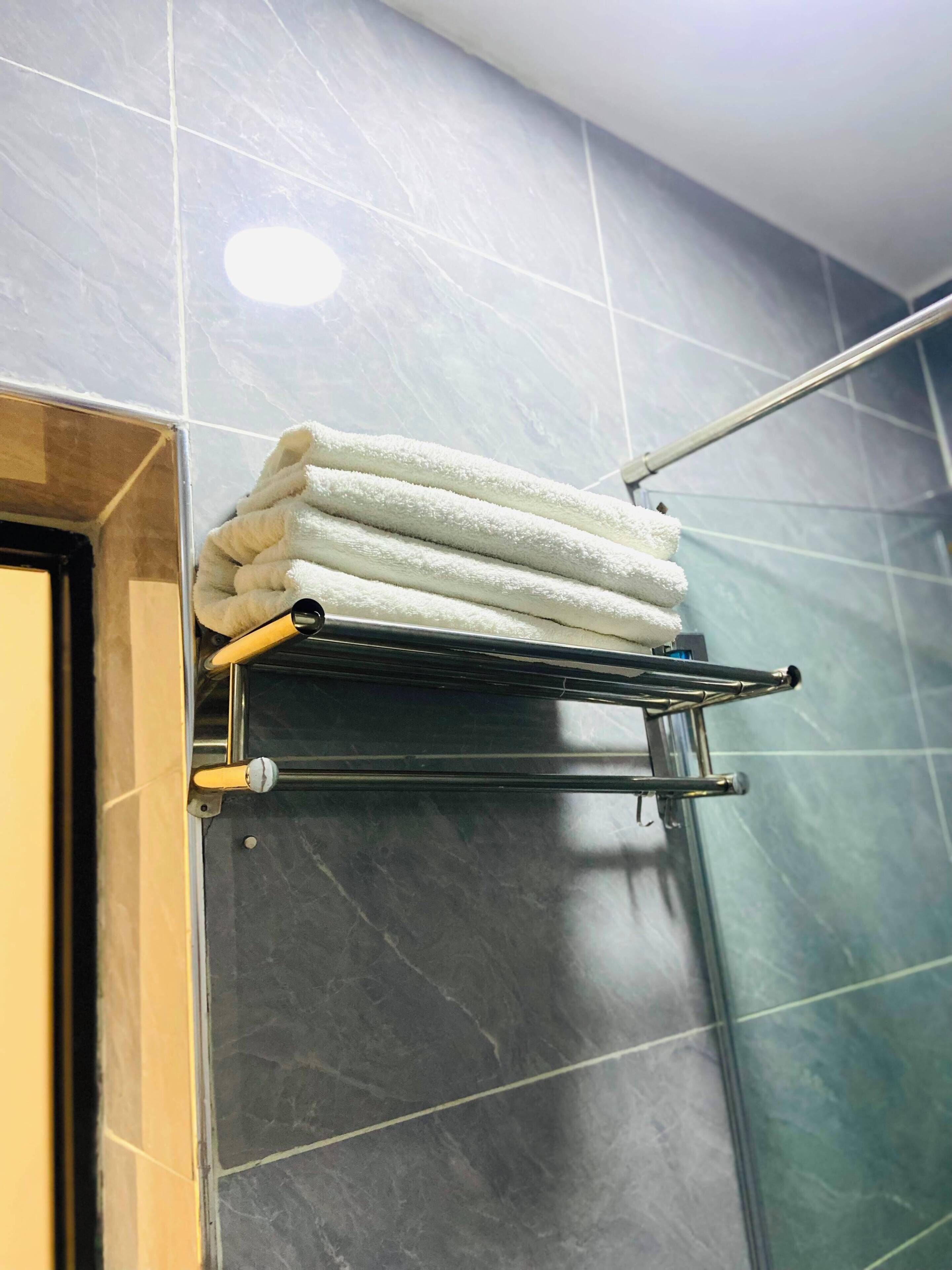 Ein Badezimmer mit Handtuchhalter, gefalteten Handtüchern, einer Duschkabine und dunklen Fliesen.