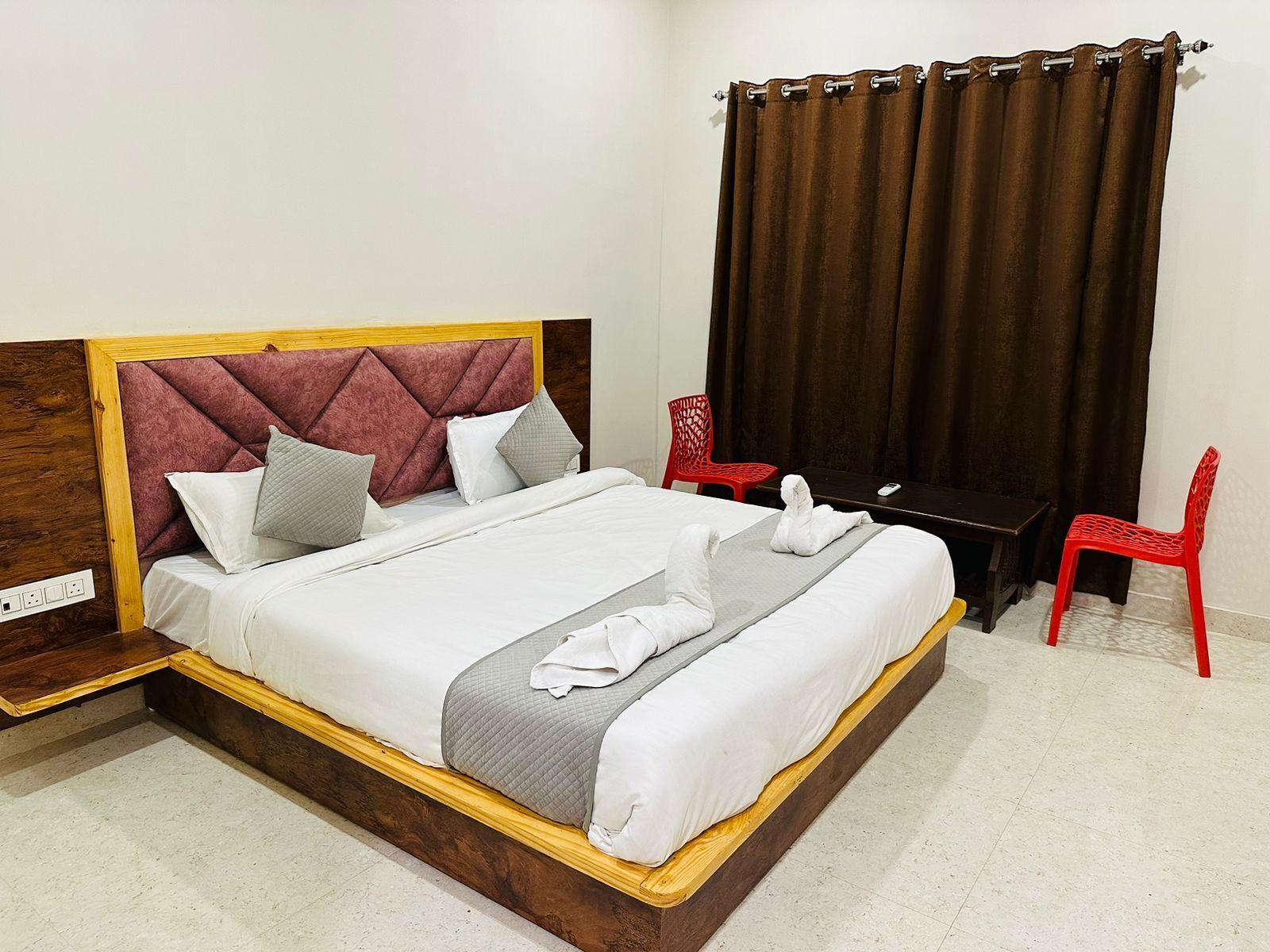 A hotel room with a bed, a desk, two red chairs, and a curtain.