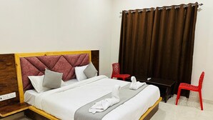 Une chambre d’hôtel avec un lit, un bureau, deux chaises rouges et un rideau.