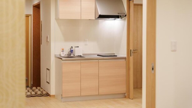 A compact kitchen with wooden cabinets, a stainless steel range hood, and a countertop with a kettle and a small appliance. - Direct train access to 道頓堀 黒門市場 USJ Kyoto Temmabashi Blue Sky Guesthouse (Osaka)