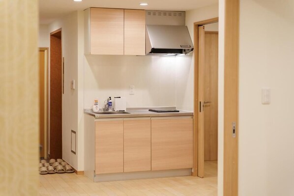 A compact kitchen with wooden cabinets, a stainless steel range hood, and a countertop with a kettle and a small appliance.