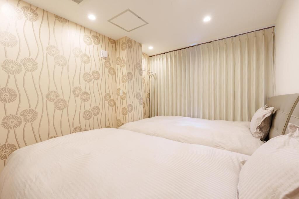 A hotel room with a large bed, a headboard, a window with curtains, and a wall with a floral pattern.