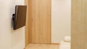 A room with a wooden door, a white sofa, and a mounted television. - Direct train access to 道頓堀 黒門市場 USJ Kyoto Temmabashi Blue Sky Guesthouse (Osaka)