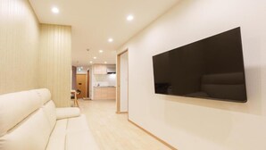 A modern hotel room with a sofa, a flat-screen TV mounted on the wall, and a wooden floor. - Direct train access to 道頓堀 黒門市場 USJ Kyoto Temmabashi Blue Sky Guesthouse (Osaka)