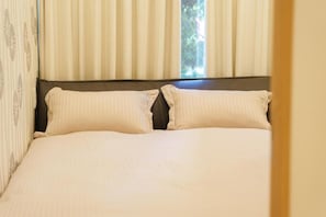 A bed with a headboard and two pillows, a window with curtains, and a partial view of a wall.