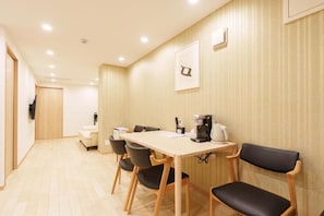 A hotel room with a wooden floor, a dining table with chairs, a coffee maker, and a TV mounted on the wall.