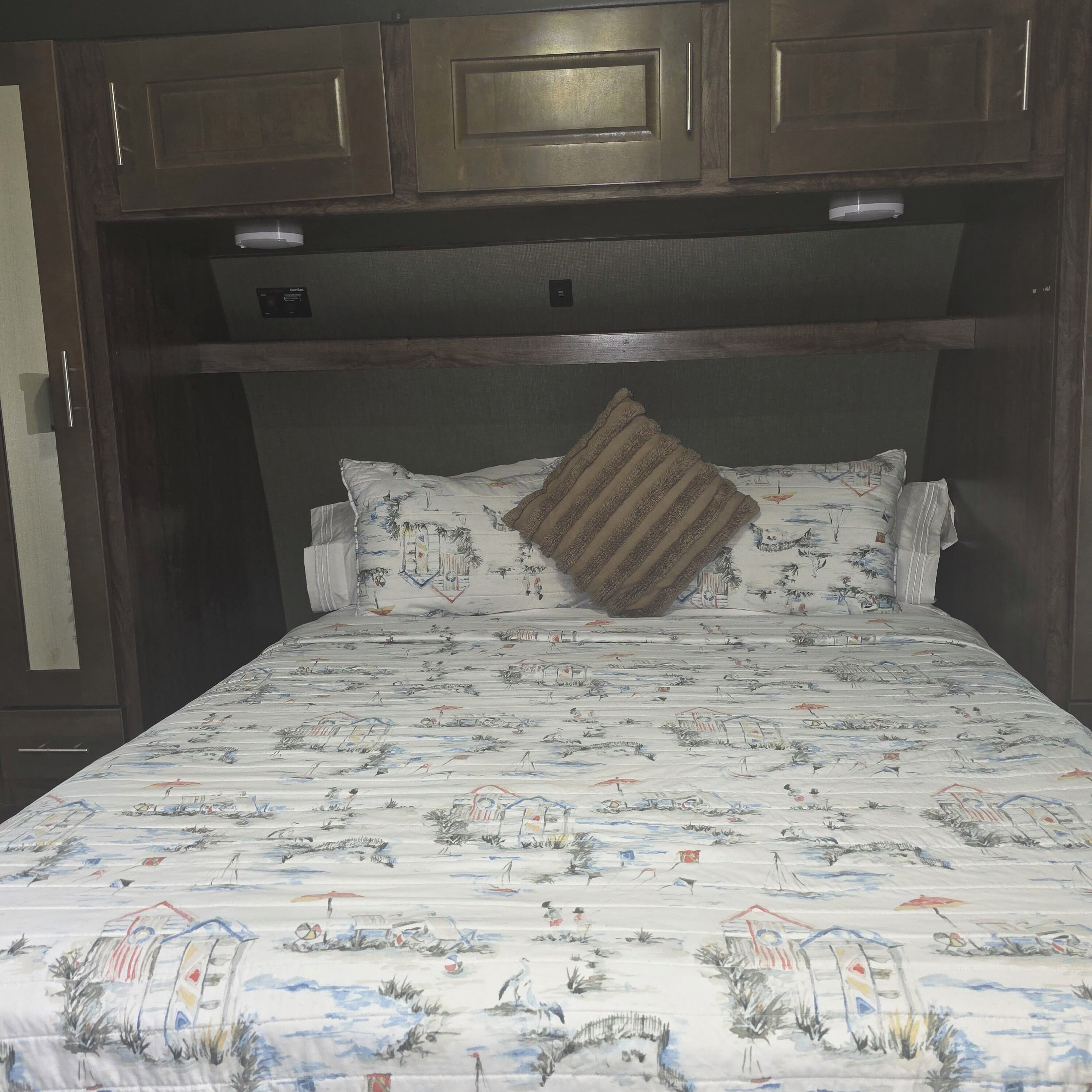 A bed with a patterned bedspread, wooden headboard, and a single decorative pillow.