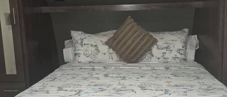A bed with a patterned bedspread, wooden headboard, and a single decorative pillow.