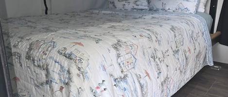 A bed with a patterned bedspread, a headboard, and a window with blinds.