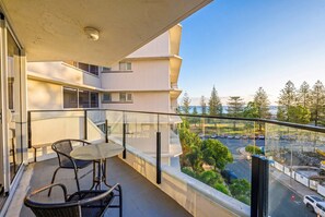 A balcony with a table and chairs, overlooking a parking area and trees. - "HAVEN" By TheGuestHouse. (Broadbeach)