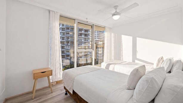 Ein Schlafzimmer mit zwei Betten, einem Deckenventilator und Blick auf ein Gebäude durch das Fenster.