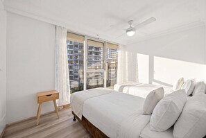 Ein Schlafzimmer mit zwei Betten, einem Deckenventilator und Blick auf ein Gebäude durch das Fenster.