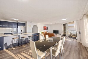 A modern kitchen with a central island, bar stools, and a dining area with a glass table and chairs. - "HAVEN" By TheGuestHouse. (Broadbeach)