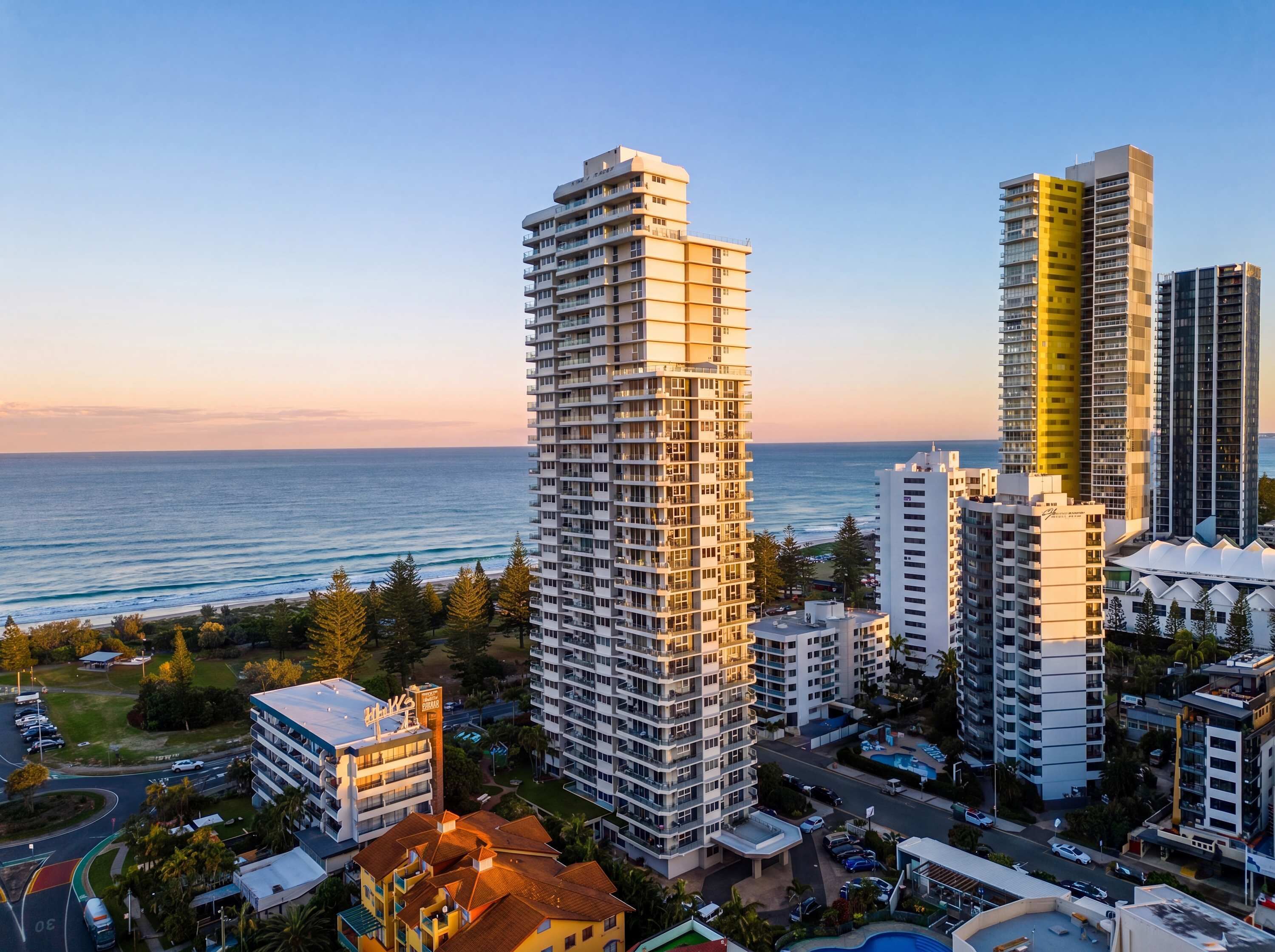 A high-rise building with multiple floors, a parking area, and a view of the ocean.
