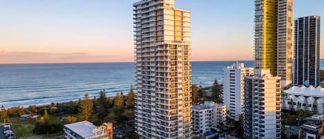 A high-rise building with multiple floors, a parking area, and a view of the ocean.