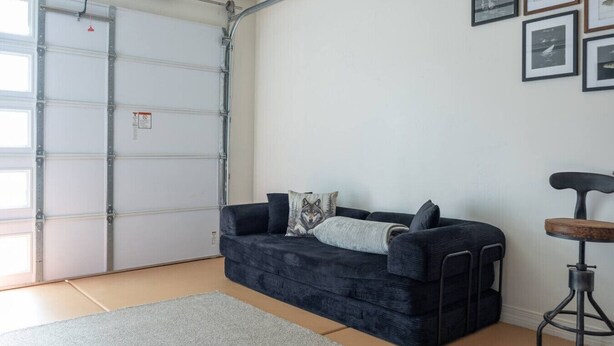 Een kamer met een grijze bank, een klein rond tafeltje en een garage deur.