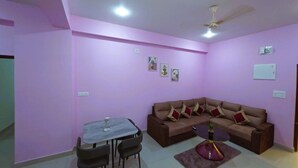 A living room with a brown sofa, a dining table with chairs, and a ceiling fan. - A Boutique Hotel (Bhubaneshwar)