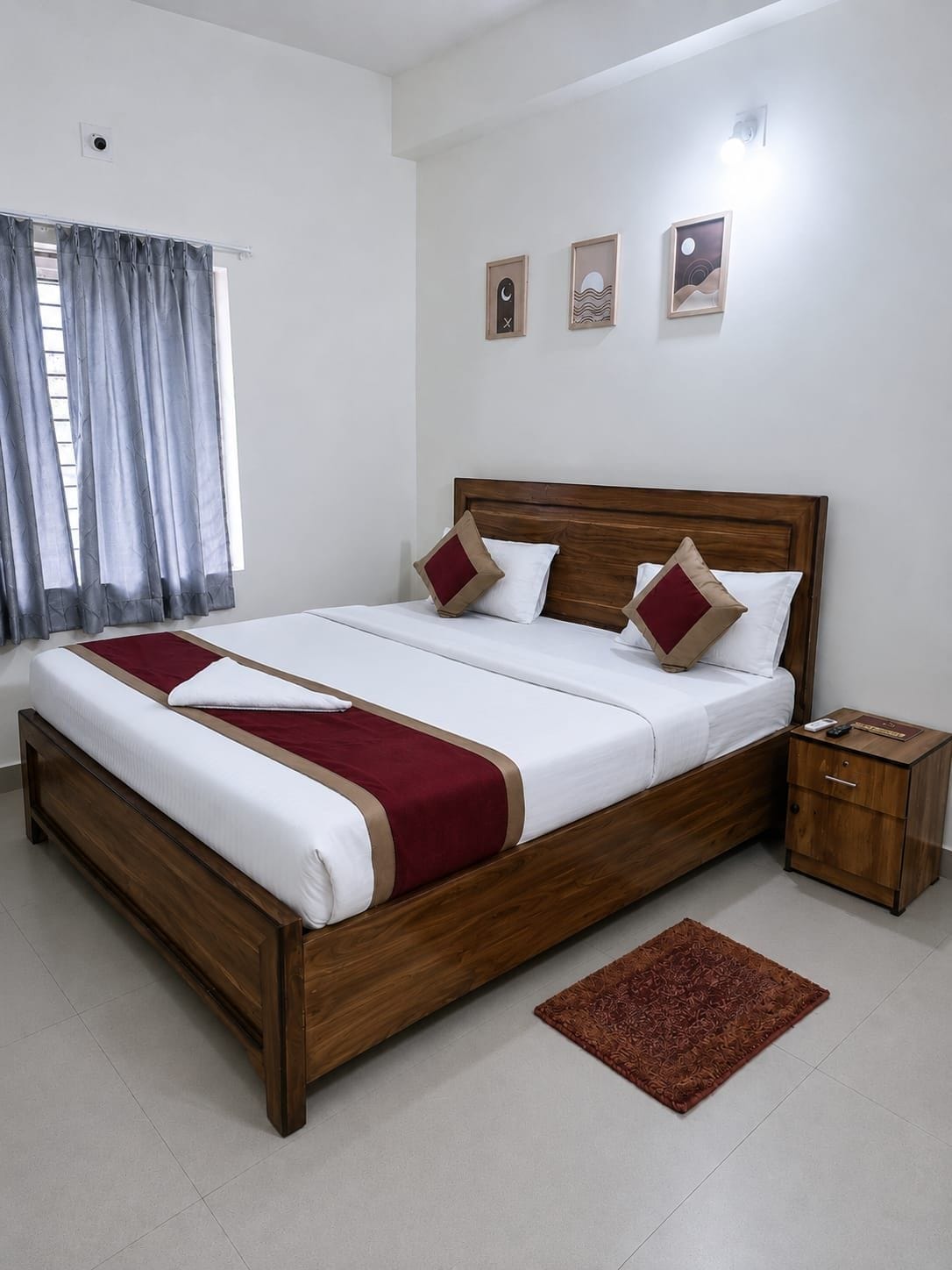Una cama bien hecha con estructura de madera y ropa blanca, una mesita de noche con lámpara, y una alfombra estampada en el suelo.