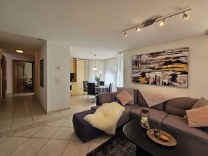 A modern living room with a sofa, a coffee table, and a dining area in the background. - Chateau EG by Interhome (Saas-Fee)