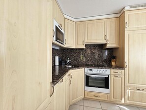 A kitchen with wooden cabinets, a granite countertop, a microwave, a stove, and a tiled backsplash. - Chateau EG by Interhome (Saas-Fee)