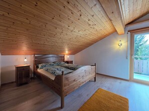 Ein Schlafzimmer mit schrägen Wänden, einem hölzernen Bett, Nachttischen und einem Fenster mit Blick.