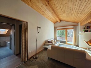 A cozy room with a wooden ceiling, a sofa, a floor lamp, and a view through a large window. - Vallesia Penthouse by Interhome (Saas-Fee)