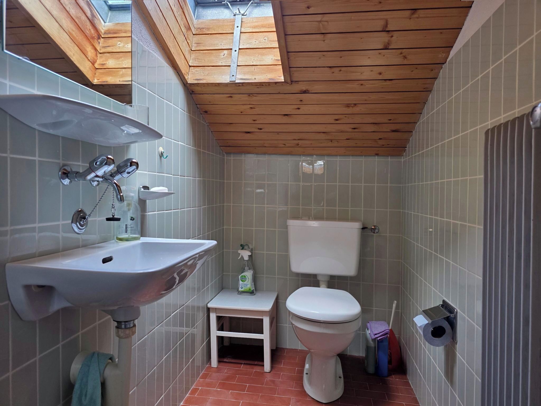A bathroom with a skylight, a sink, a toilet, and a small step stool.
