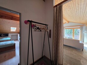 Ein Zimmer mit einem Bett, einem Heizkörper, einer Holzbalkendecke, einem Fenster und einer Tür zu einem anderen Raum.