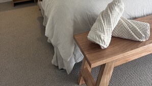 A neatly made bed with a wooden headboard, a bedside table, and a bench with towels. - Aelia in Peregian Beach (Peregian Beach)