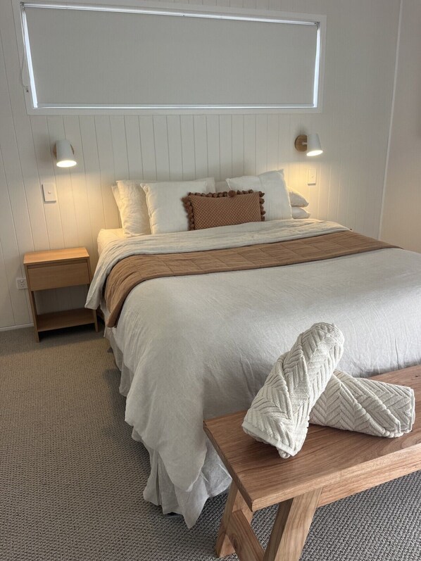 A neatly made bed with a wooden headboard, a bedside table, and a bench with towels.