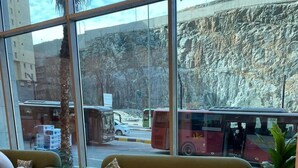 Een modern interieur met een bank, fauteuils, grote ramen en uitzicht op een straat met bussen.