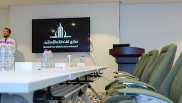 A conference room with a presentation screen, a table with water bottles, and green upholstered chairs.