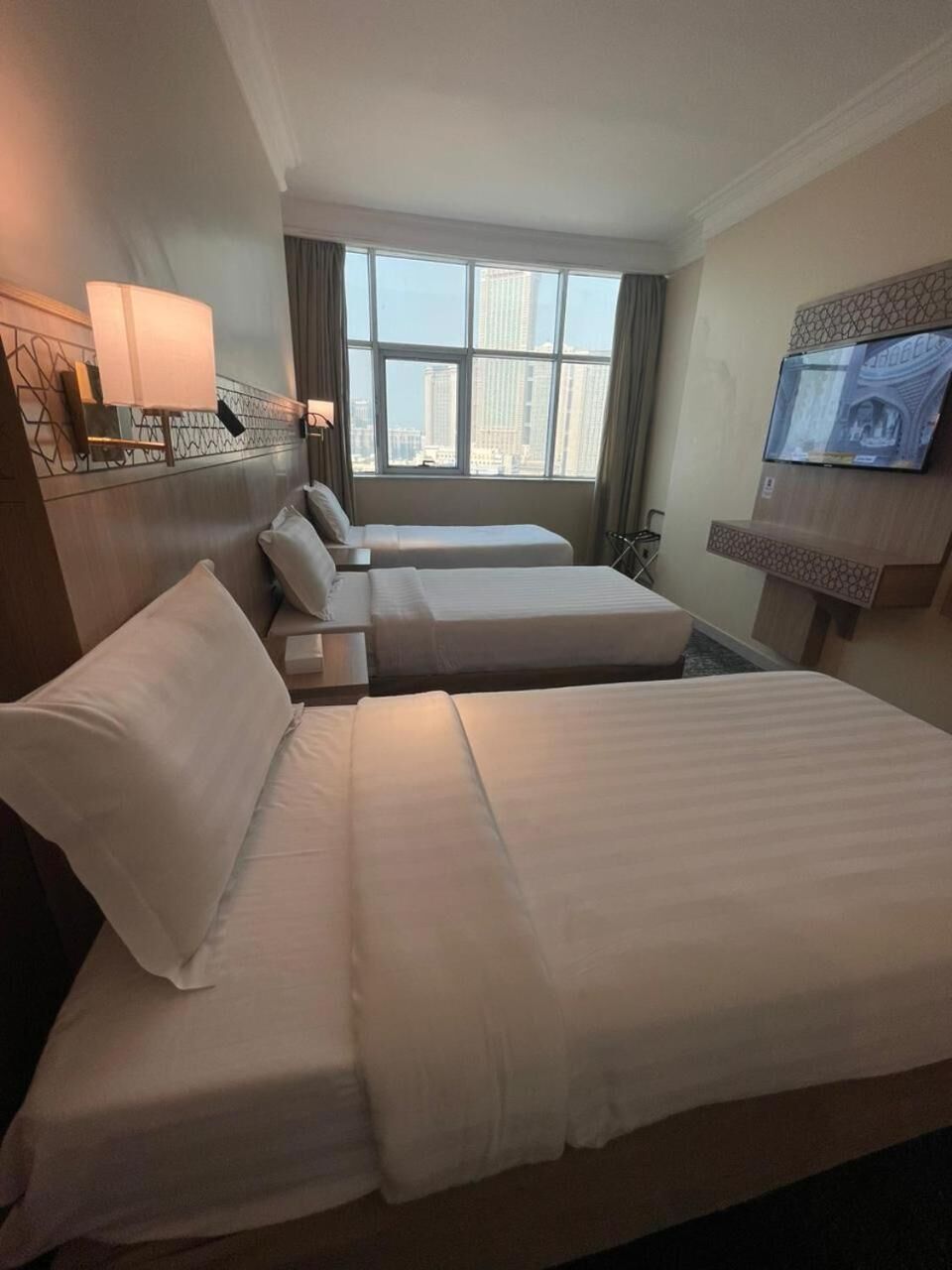 Une chambre d’hôtel avec un grand lit, deux petits lits, une télévision et une fenêtre donnant sur la ville.
