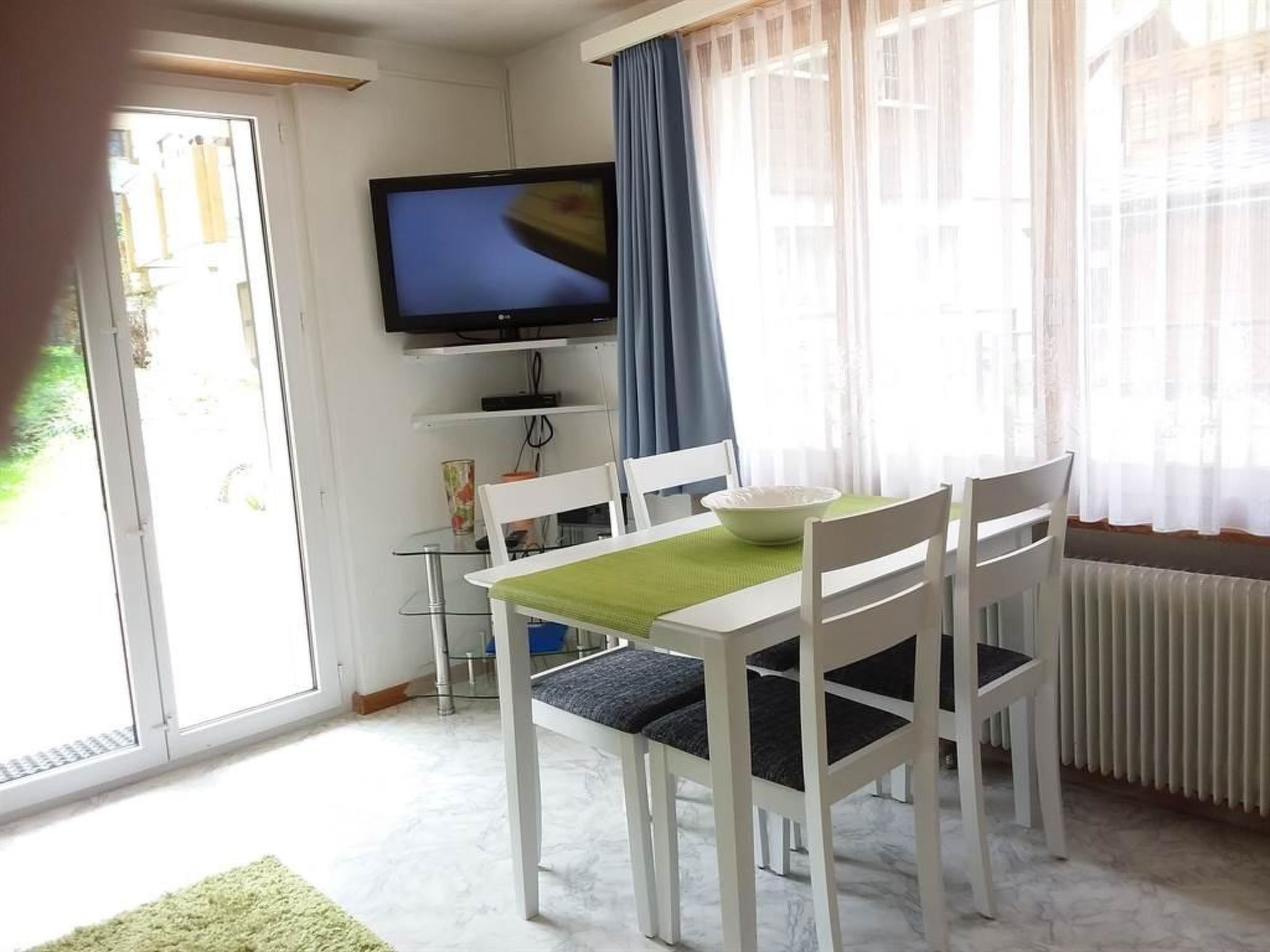 Un coin repas avec une table et des chaises, un téléviseur fixé au mur et une fenêtre avec des rideaux.