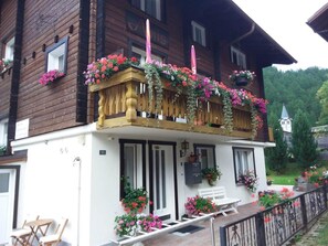 A two-story building with a balcony adorned with flowers and a wooden railing. - Apartment Anis by Interhome (Saas-Almagell)