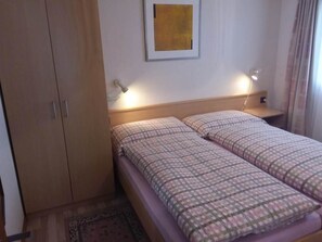 A room with a bed, a wardrobe, a nightstand, a lamp, and a painting on the wall. - Apartment Anis by Interhome (Saas-Almagell)
