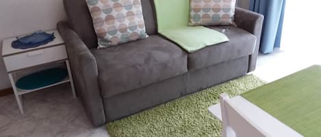 Un sofá gris con cojines estampados, una mesita auxiliar blanca y una alfombra verde.