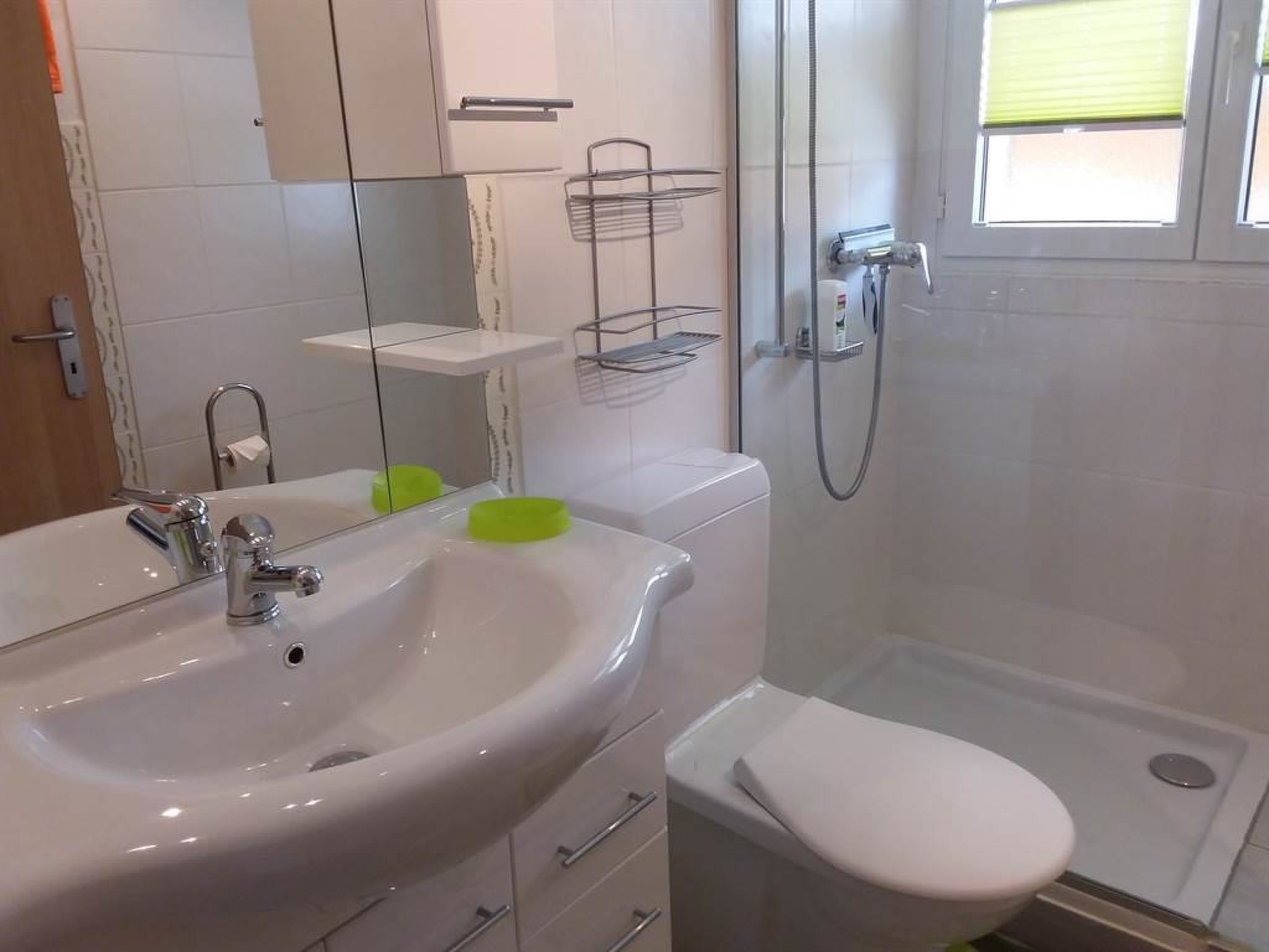 Une salle de bain avec un lavabo blanc, un miroir et des toilettes. Il y a un espace douche avec une porte en verre et un porte-serviettes.