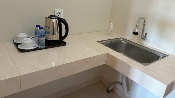 Una pequeña kitchenette con un lavamanos, un hervidor, tazas y agua embotellada.