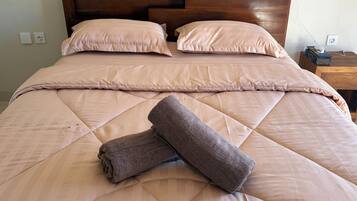 A neatly made bed with a quilted cover, two pillows, and two rolled towels.