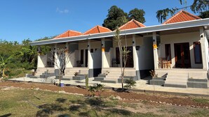 Un edificio con porche cubierto y varias puertas, rodeado de un jardín ajardinado.
