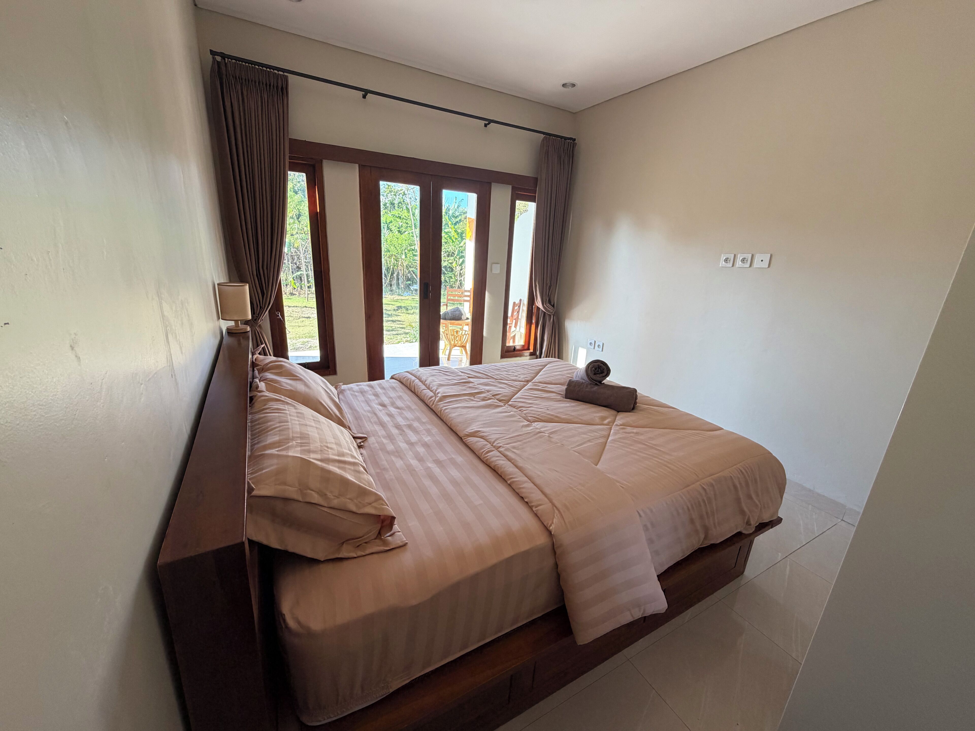 A bedroom with a bed, curtains, a window, and a view of greenery outside.