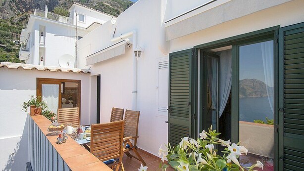 Un balcon avec une table dressée pour deux personnes, des chaises et un pot de fleurs.