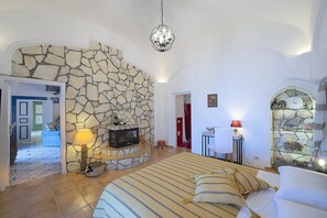 A bedroom with a stone fireplace, a bed with striped bedding, a chandelier, and a glass fish tank. - Villa Bellora: A welcoming independent house situated at a short distance from the beach, with Free WI-FI. (Praiano)