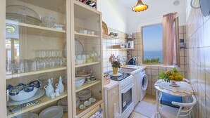 Une cuisine compacte avec vue, équipée d’une cuisinière, d’un évier et d’une fenêtre donnant sur la mer.