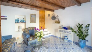Une pièce avec un plafond en bois, un sol à motifs, un canapé, une table agrémentée d’objets décoratifs et une plante en pot.