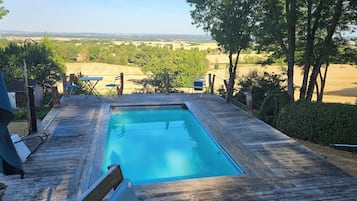 Une piscine rectangulaire avec une terrasse en bois, entourée d’arbres et offrant une vue sur la campagne.
